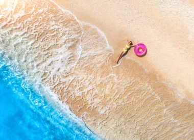 Gün batımında dalgalarla birlikte kumlu sahilde pembe yüzme yüzüğüyle uzanan genç ve güzel kadının havadan görüntüsü. Yunanistan 'ın Lefkada adasında yaz tatili. Sıska kız manzaralı, masmavi bir su.