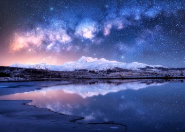 Kış gecesi, karlı dağların ve deniz kıyısının üzerinde parlak Samanyolu. Karlı kayalıklı manzara, yıldızlı gökyüzü, suda yansıma, fiyort. Lofoten Adaları, Norveç. Boşluk. Güzel Samanyolu ve yıldızlar