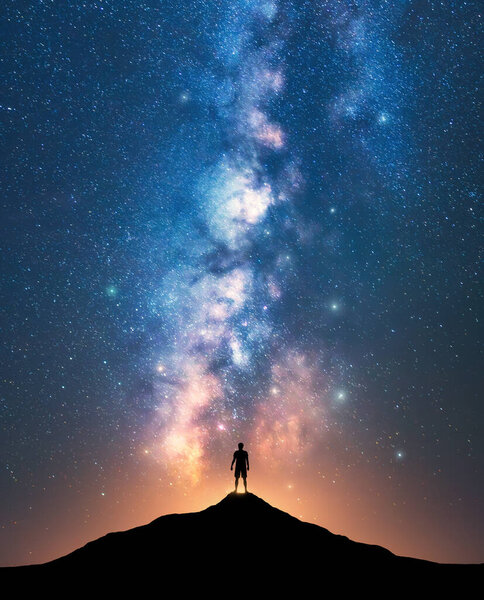 Milky Way and sporty man on mountain peak at starry night. Silhouette of a guy on the hill, sky with stars, yellow light in Nepal. Galaxy. Space landscape with bright milky way. Travel background