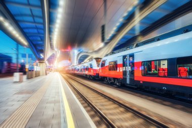 Yüksek hızlı tren gece tren istasyonunda hareket halindedir. Hareket eden kırmızı modern yolcu treni, demiryolu platformu, şehir ışıkları. Graz, Avusturya 'daki modern tren istasyonu. Demiryolu. Bulanık arkaplan