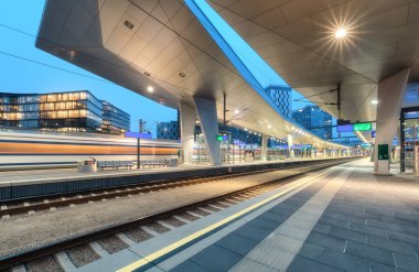 High speed train in motion on the railway station at night. Moving blue modern intercity passenger train, railway platform, architecture, city lights. Modern train station in Vienna, Austria. Railroad