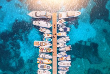 Aerial view of boats and luxure yachts in dock at sunset in summer in Sardinia, Italy. Colorful landscape with sailboats and motorboats in sea bay, jatty, clear blue sea. Top view of harbor. Travel