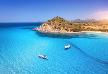 Yazın günbatımında mavi denizde lüks yatların hava manzarası. Sardunya, İtalya. Sürat tekneleri, yatları, deniz lagünü, dağı, şeffaf gök mavisi suyu ve gökyüzü olan tropik deniz manzarası. Üst İHA görünümü