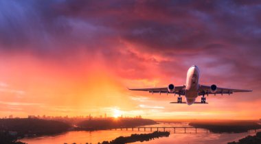 Uçak gün batımında şehrin üzerinde renkli gökyüzünde uçuyor. Yolcu uçağıyla manzara, ufuk çizgisi, alacakaranlıkta kırmızı ve pembe bulutlu mor gökyüzü. Uçak alacakaranlıkta iniyor. Uçağın hava görüntüsü
