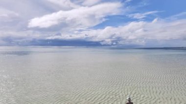 Okyanustaki kumsalda genç bir kadının havadan görünüşü, beyaz kum, mavi deniz, güneşli yaz gününde Zanzibar adasında. Kızın üst görüntüsü, kum tükürüğü, körfez, bulutlar berrak suya yansıyan bulutlar.