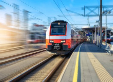 Yüksek hızlı kırmızı yolcu treni gün batımında açık mavi gökyüzünün altında tren istasyonunda hareket ediyor. Tren istasyonu. Bulanık hareket etkisine sahip modern demiryolu taşımacılığı konsepti. Demiryolu. Ticari.