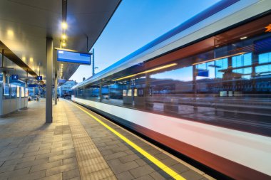 Yüksek hızlı yolcu treni gece aydınlık tren istasyonunda hareket halindedir. Hareket eden modern şehirler arası tren, demiryolu platformu, mimari, ışıklar. Graz, Avusturya 'daki tren istasyonu. Demiryolu.