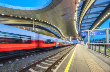 Yüksek hızlı yolcu treni gece aydınlık tren istasyonunda hareket halindedir. Hareket eden kırmızı modern şehirler arası tren, demiryolu platformu, mimari, ışıklar. Graz, Avusturya 'daki tren istasyonu. Demiryolu.