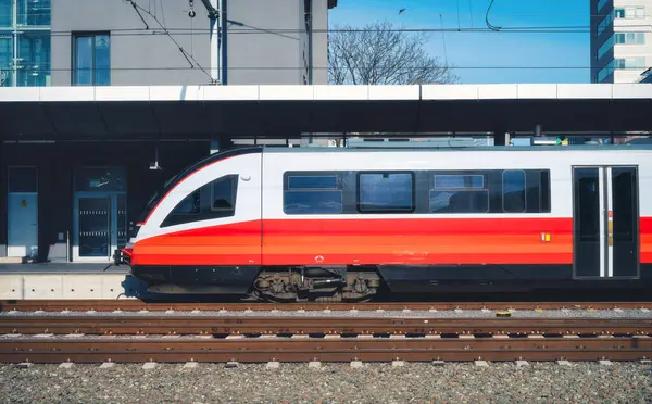 Gün batımında açık mavi gökyüzünün altındaki tren istasyonunda yüksek hızlı kırmızı yolcu treni. Tren istasyonu. Modern demiryolu taşıma konsepti. Demiryolu. Reklam. Avusturya 'da demiryolu taşımacılığı