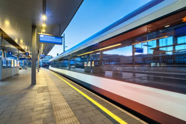 Yüksek hızlı yolcu treni gece aydınlık tren istasyonunda hareket halindedir. Hareket eden modern şehirler arası tren, demiryolu platformu, mimari, ışıklar. Graz, Avusturya 'daki tren istasyonu. Demiryolu.