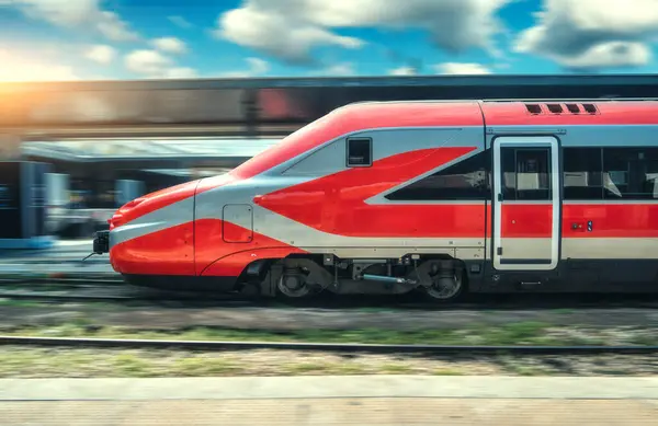 stock image High-speed red passenger train moving at railway station platform under clear blue sky at sunset. Train station. Modern railway transportation concept with blurred motion effect. Railroad. Commercial