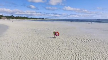 Zanzibar adasında güneşli bir yaz gününde yüzme yüzüğü, kumlu plaj, mavi deniz manzaralı sportif bir kadın. Güzel kız manzarası, kumsal, okyanus, bulutlu gökyüzü, palmiyeler