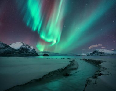 Kuzey Işıkları, karlı dağlar, kumlu plaj, yıldızlı kış gecesinde dere. Lofoten Adaları, Norveç. Muhteşem Aurora Borealis. Kutup ışıklarıyla gökyüzü. Aurora, deniz, dere, kardaki kayalar