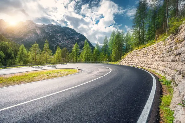 Yazın gün batımında dağlarda yol. Dolomitler, İtalya. Güzel yol, yeşil kadın, yüksek kayalar, bulutlu mavi gökyüzü. Baharda dağ geçidinden geçen içi boş otoban manzarası. Seyahat