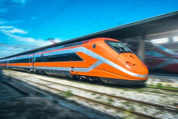 stock image High-speed orange passenger train moving at railway station platform at sunset. Train station. Modern railway transportation concept with blurred motion effect. Railroad. Commercial transport