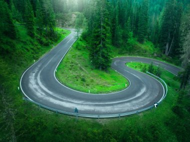 Yazın ıslak kıvrımlı yol ve yeşil ormanın havadan görünüşü. Dolomitler, İtalya. Dönek dağ yolu manzarası, ağaçlar, yağmurlu bir günde çimenler. Ormandan geçen yol. Karmaşık bir manzarası var. Alpler