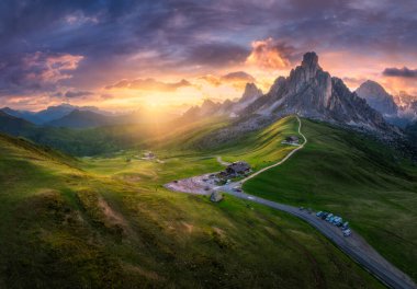 Dağ vadisindeki yol manzarası, yazın günbatımında altın güneş ışığı. Passo Giau, Dolomitler, İtalya. Güzel kayaların manzarası, yeşil çimenler, alp çayırları, dağ zirveleri, mor gökyüzü. Doğa