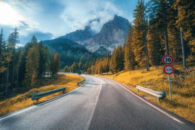 Sonbaharda gün batımında Alp dağlarında yol. Dolomitler, İtalya. Güzel yol, turuncu kadın, bulutlardaki yüksek kayalar. Sonbaharda dağ geçidinde içi boş otoban manzarası. Seyahat et. Aktarım