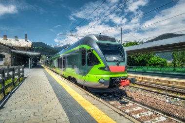 Gün batımında mavi gökyüzünün altındaki tren istasyonunda yüksek hızlı yeşil yolcu treni. Dağ tren istasyonu. Modern demiryolu taşıma konsepti. Demiryolu. Reklam. İtalya 'da demiryolu taşımacılığı