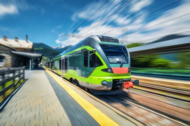 Yüksek hızlı yeşil yolcu treni gün batımında tren istasyonunda hareket ediyor. Tren istasyonu. Bulanık hareket etkisine sahip modern demiryolu taşımacılığı konsepti. Demiryolu. Ticari ulaşım