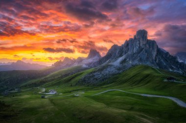 Dağ vadisinde yol, altın güneş ışığı ve yazın günbatımında bulutlarla dolu renkli gökyüzü. Seyahat et. Passo Giau, Dolomitler, İtalya. Güzel kayalar, yeşil çimenler, alp çayırları, dağ zirveleri. Doğa