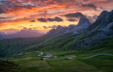 Dağ vadisinde yol, altın güneş ışığı ve yazın günbatımında bulutlarla dolu renkli gökyüzü. Seyahat et. Passo Giau, Dolomitler, İtalya. Güzel kayalar, yeşil çimenler, alp çayırları, dağ zirveleri. Doğa