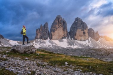 Yazın günbatımında taşın üzerinde sırt çantası ve yüksek dağ zirveleri olan bir kız. Tre Cime, Dolomitler, İtalya. Genç kadınla manzara, patika, kayalar, bulutlu gökyüzü ve güneş ışığı. Yürüyüş. Seyahat