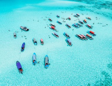 Renkli teknelerin havadan görünüşü, yazları gök mavisi suyla kaplı deniz koyları. Mnemba Adası, Zanzibar. Düşük gelgit, mavi deniz, kum, yüzen insanlar, yatlar. Okyanus. Kristal berraklığında göl