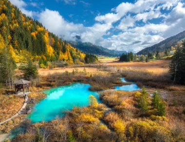 Gök mavisi gölü, portakal ormanı ve sonbaharda günbatımında çimen manzarası. Zelenci Gölü, Slovenya, Triglav Ulusal Parkı. Güzel göl manzarası, dağlar, ağaçlar, sonbaharda bulutlu gökyüzü. Peyzaj