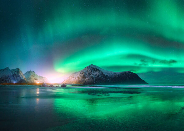 Northern Lights and beach in Lofoten islands, Norway. Beautiful Aurora borealis. Starry sky with polar lights. Night winter landscape with aurora, sea with sky reflection in water, snowy mountains