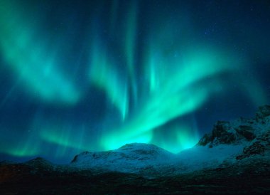 Norveç 'in Lofoten kentindeki karlı dağların üzerindeki kuzey ışıkları. Karların üzerindeki Aurora borealis kayaları kapladı. Kutup ışıklarıyla kış manzarası, dağ zirvesi. Parlak aurora ile parıltılı gökyüzü