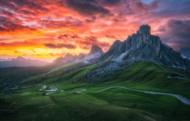 Dağ vadisinde yol, altın güneş ışığı ve yazın günbatımında bulutlarla dolu renkli gökyüzü. Seyahat et. Passo Giau, Dolomitler, İtalya. Güzel kayalar, yeşil çimenler, alp çayırları, dağ zirveleri. Doğa