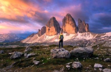 Sonbaharda gün batımında taşın üzerinde sırt çantası ve yüksek dağ zirveleri olan bir kız. Tre Cime, Dolomitler, İtalya. Genç kadınla manzara, patika, kayalar, sonbaharda bulutlu gökyüzü. Yürüyüş. Seyahat