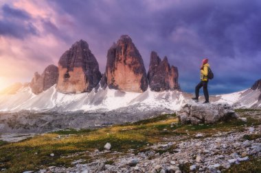 Sonbaharda gün batımında taşın üzerinde sırt çantası ve yüksek dağ zirveleri olan bir kız. Tre Cime, Dolomitler, İtalya. Genç kadınla manzara, patika, kayalar, sonbaharda bulutlu gökyüzü. Yürüyüş. Seyahat