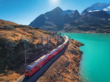 Gök mavisi Bianco Gölü yakınlarındaki modern kırmızı trenin havadan görünüşü, sonbaharda günbatımında karlı kayalar ve mavi gökyüzü. Bernina Express, İsviçre. Alplerdeki tren manzarası, demiryolu, sonbaharda turuncu tepeler