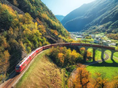 Sonbaharda gün batımında Kreisviadukt 'taki Alp Dağları' ndaki kırmızı trenin hava manzarası. Bernina Express, İsviçre. Tren manzarası, demiryolu, yeşil çimenler, sonbaharda renkli ağaçlar. the Spiral viyadük
