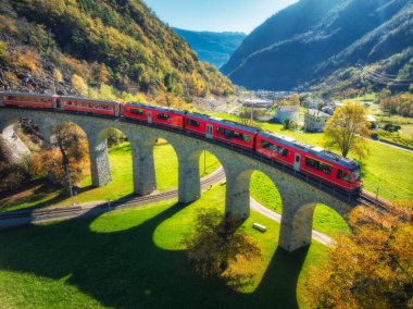 Sonbaharda gün batımında Kreisviadukt 'taki Alp Dağları' ndaki kırmızı trenin hava manzarası. Bernina Express, İsviçre. Tren manzarası, demiryolu, yeşil çimenler, sonbaharda renkli ağaçlar. the Spiral viyadük