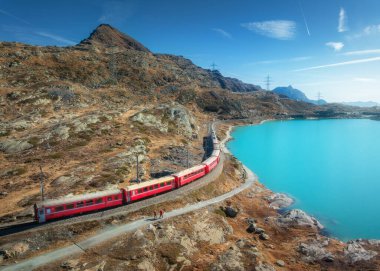 Gök mavisi Bianco Gölü yakınlarındaki modern kırmızı trenin havadan görünüşü, sonbaharda gün doğumunda karlı kayalar ve mavi gökyüzü. Bernina Express, İsviçre. Alplerdeki tren manzarası, demiryolu, sonbaharda turuncu tepeler