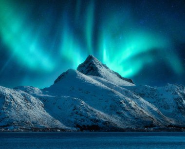 Norveç 'in Lofoten kentindeki karlı dağların üzerindeki kuzey ışıkları. Karların üzerindeki Aurora borealis kayaları ve denizi kaplamıştı. Kutup ışıklarıyla kış manzarası, dağ zirvesi. Aurora ile yıldızlı gökyüzü