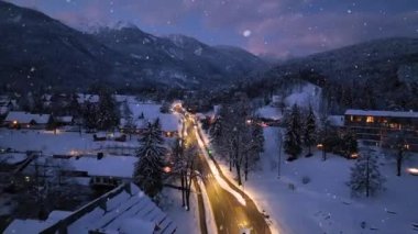 Kış perisi gecesinde peri ormanlarındaki dağ yolunun hava manzarası. Dağ köyü, evler, aydınlanma, otoyol, arabalar, güzel Slovenya 'da alacakaranlıkta karlı çam ağaçları.