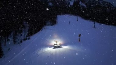 Kar yağışı altında, kar yağışı altında, kar yamacındaki kar arabasının hava görüntüsü. Kranjska Gora, Slovenya. Kar temizleme, kayak merkezi, alacakaranlıkta ışıklar. Kar temizleme makinesi