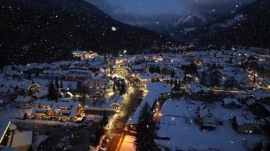 Kar yağışı altındaki güzel kayak merkezinin havadan görünüşü. Kranjska Gora, Slovenya soğuk kış gecesinde. Kardaki binaların, şehir ışıklarının, yolların, karlı dağların, alacakaranlıktaki gökyüzünün en yüksek insansız hava aracı görüntüsü. Triglav Parkı