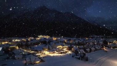 Kar yağışı altındaki güzel kayak merkezinin havadan görünüşü. Kranjska Gora, Slovenya soğuk kış gecesinde. Kardaki binaların, şehir ışıklarının, yolların, karlı dağların, alacakaranlıktaki gökyüzünün en yüksek insansız hava aracı görüntüsü. Triglav Parkı