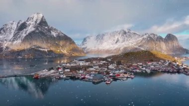 Karlı dağın havadan görünüşü, deniz, deniz, su, yol, kar yağışında gün batımında bulutlu bulutların yansıması. Norveç, Lofoten adalarındaki Reine köyünün güzel insansız hava aracı manzarası