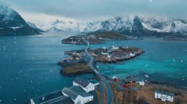 Karlı dağların havadan görünüşü, daha büyük evleri olan adalar, mavi deniz, köprü, yol, kışın bulutlu gökyüzü. Norveç 'in Lofoten adalarındaki Reine köyünün insansız hava aracı görüntüsü. Dramatik