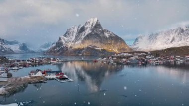 Karlı dağın havadan görünüşü, deniz, deniz, su, yol, kar yağışında gün batımında bulutlu bulutların yansıması. Norveç, Lofoten adalarındaki Reine köyünün güzel insansız hava aracı manzarası