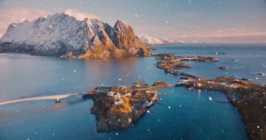 Karlı dağların havadan görünüşü, daha büyük evleri olan adalar, deniz, köprü, yol, kar yağışında gün doğumunda bulutlu gökyüzü. Norveç 'in Lofoten adalarındaki Reine ve Hamnoy köylerinin insansız hava aracı görüntüsü