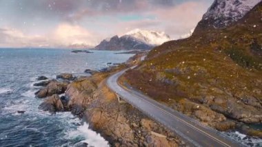 Köprü manzarası, dalgalı deniz ve kışın kar altında gün batımında karlı dağlar. Lofoten Adaları, Norveç. Güzel yol, su, kayalar, şafak vakti bulutlu pembe gökyüzü.