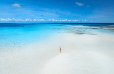 Zanzibar adasındaki Nakupenda 'da güneşli bir yaz gününde, kumsalda yalnız genç bir kadın, beyaz kum, mavi deniz manzarası. Kız manzarası, kum tükürüğü, su, bulutlu gökyüzü.