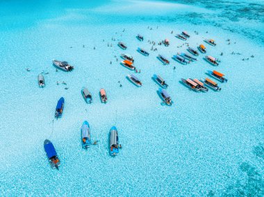 Renkli teknelerin havadan görünüşü, yazları gök mavisi suyla kaplı deniz koyları. Mnemba Adası, Zanzibar. Düşük gelgit, mavi deniz, kum, yüzen insanlar, yatlar. Okyanus. Kristal berraklığında göl